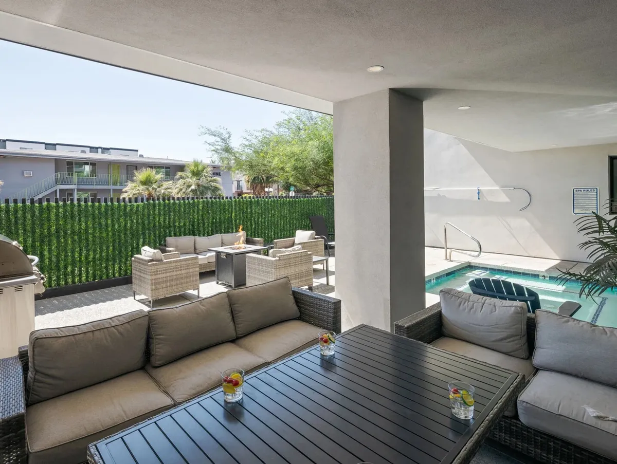 A vibrant outdoor seating area next to a swimming pool, bordered by a lush green hedge. The space is set up for relaxation and socializing, with comfortable chairs and a casual, inviting atmosphere that encourages guests and their pets to enjoy the outdoors together.