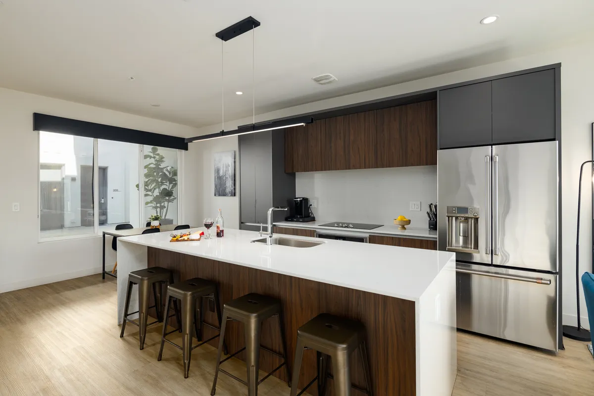 A sleek, modern kitchen featuring a central island with bar stools and high-end stainless steel appliances. The setup is ideal for cooking, casual dining, or gathering with friends, with a relaxed, contemporary feel that aligns with the 'gourmet kitchen' description.