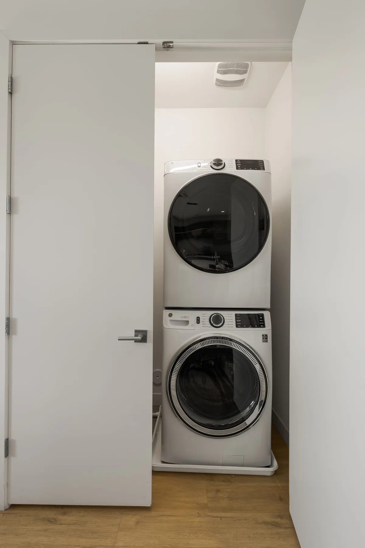 A modern, efficient laundry nook with a stacked washer and dryer, set behind a smooth white door. The surrounding area is sleek and uncluttered, highlighting convenience and thoughtful design for everyday living.