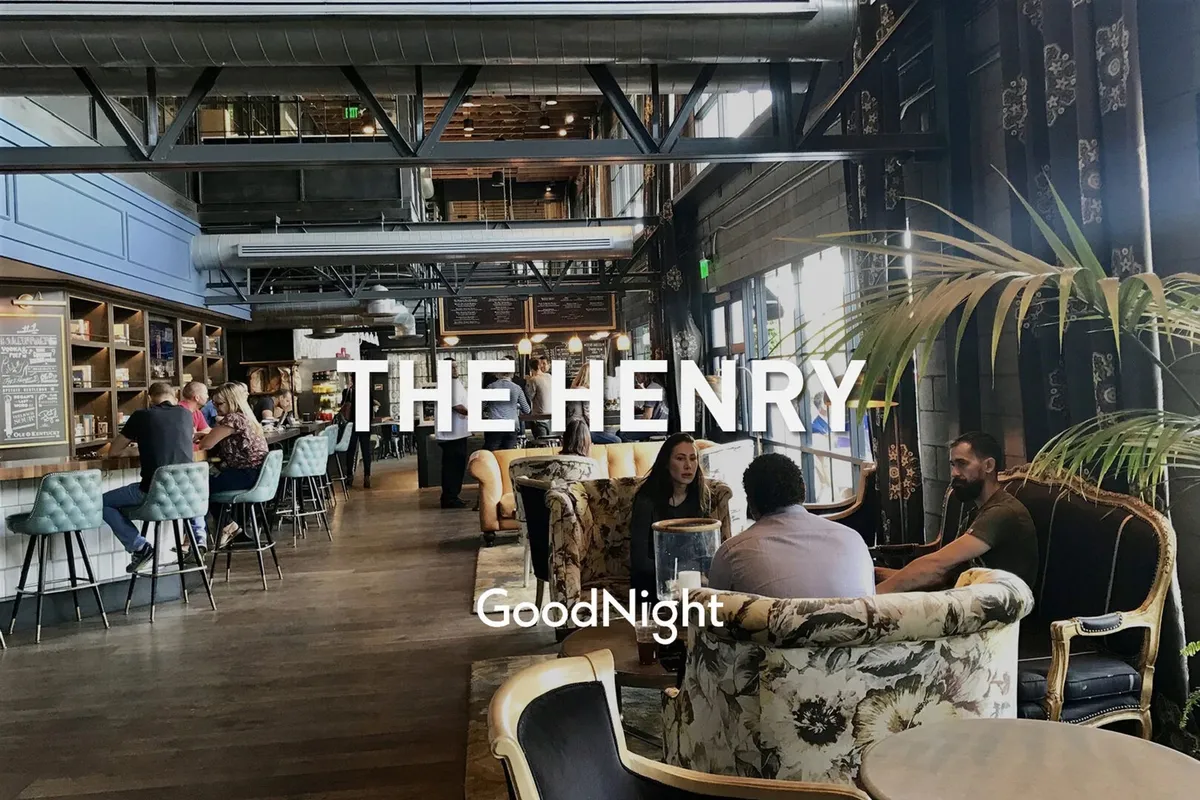 A lively interior bar area with floral upholstered seating, large windows letting in daylight, and a decorative wall. The scene is set for casual dining or networking, with an inviting, social atmosphere ideal for business travelers looking to unwind or make new connections.