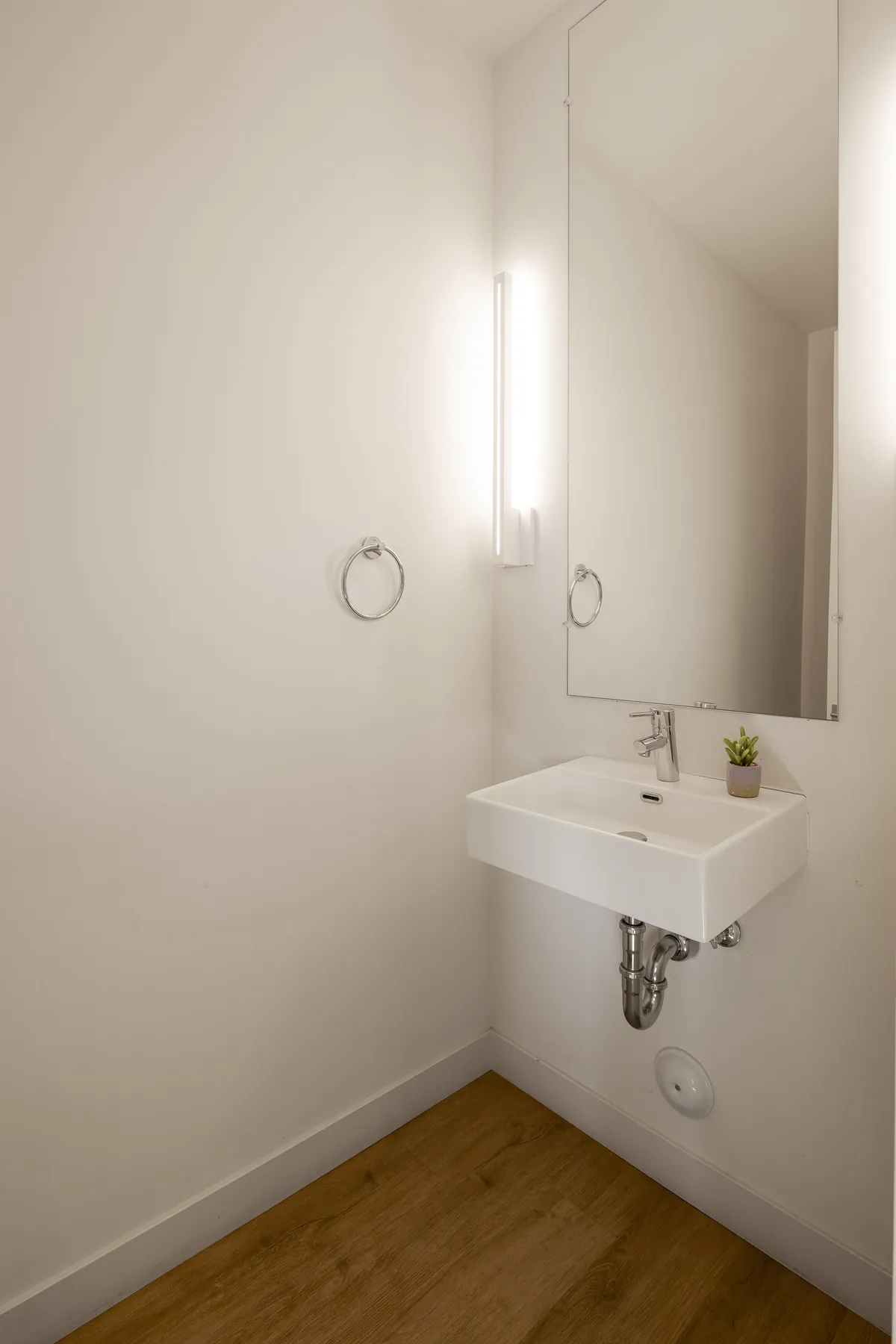 A minimalist bathroom with a modern sink, stylish mirror, subtle lighting, and a touch of greenery. The serene, uncluttered setting hints at provided bath amenities and a restful retreat.