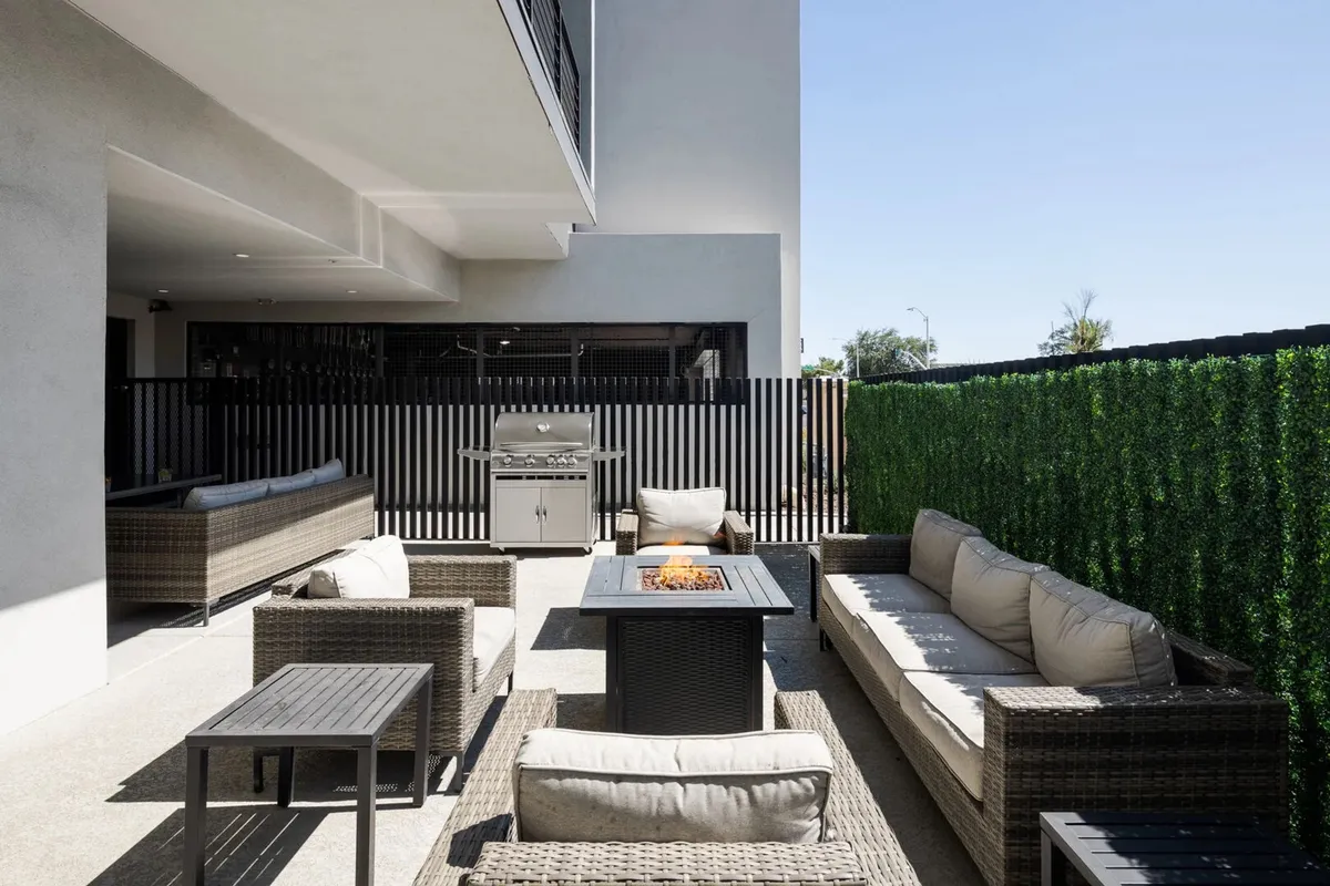 An exterior communal area featuring a cozy fire pit, grilling station, and outdoor seating. Lush hedges provide privacy, while the inviting setup is perfect for BBQs and evening gatherings by the fire.